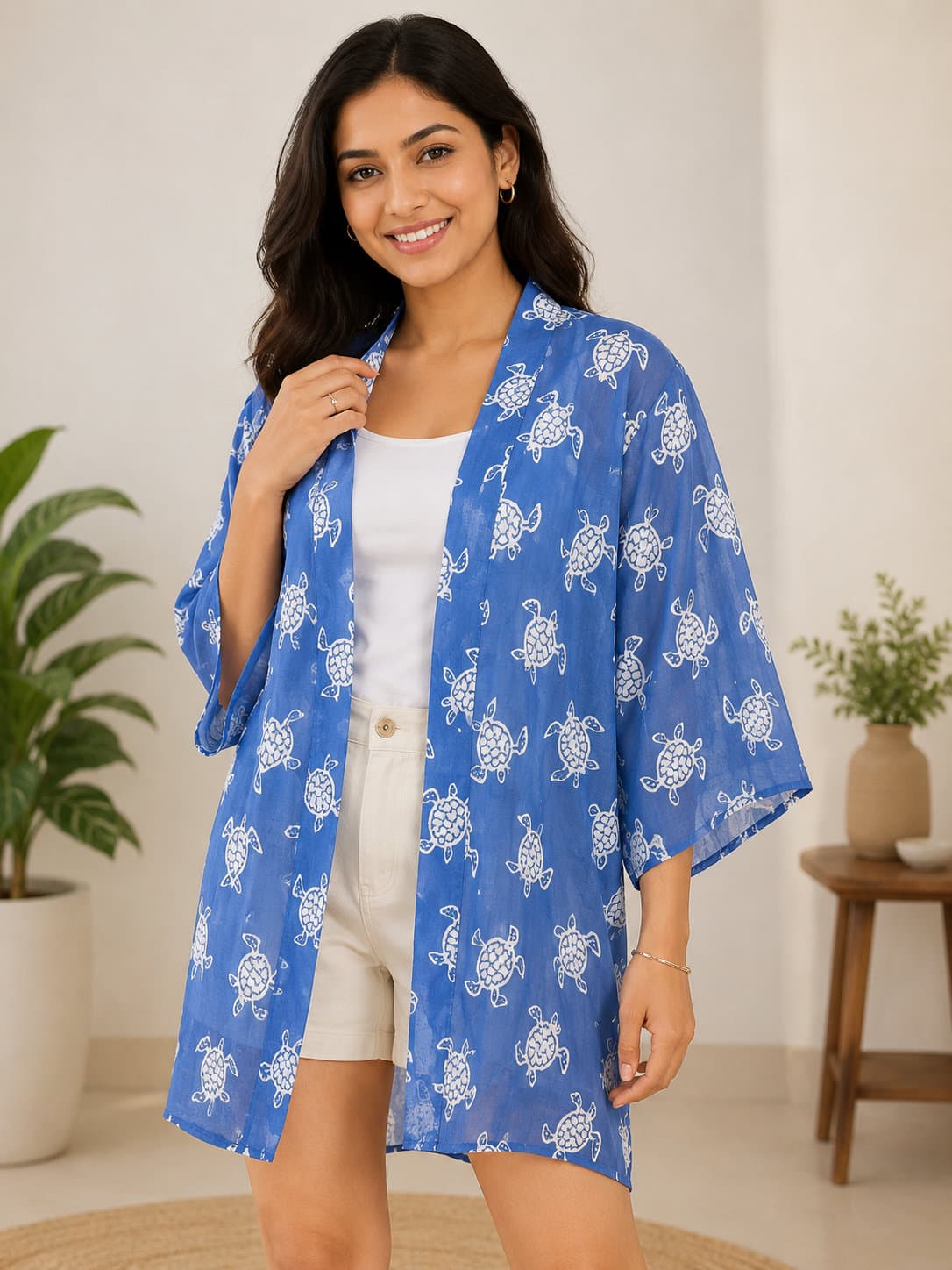 Smiling woman wearing a blue open-front kimono with white sea turtle patterns and white shorts.